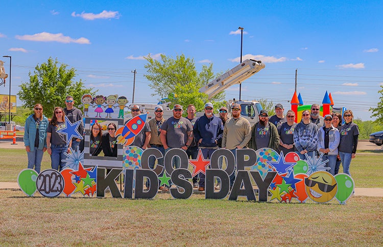 The Co-op crew poses with Co-op Kids day signage at Co-op Kids Day.